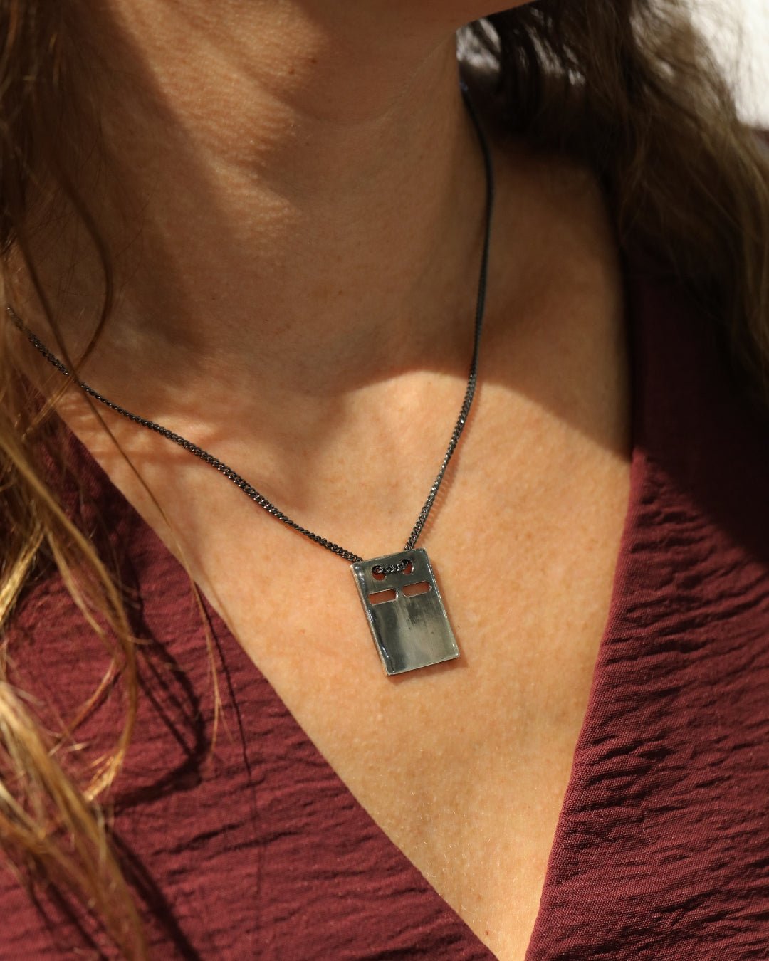 Close up of irregular rectangular silver ID bricka pendant on a dark chain against skin