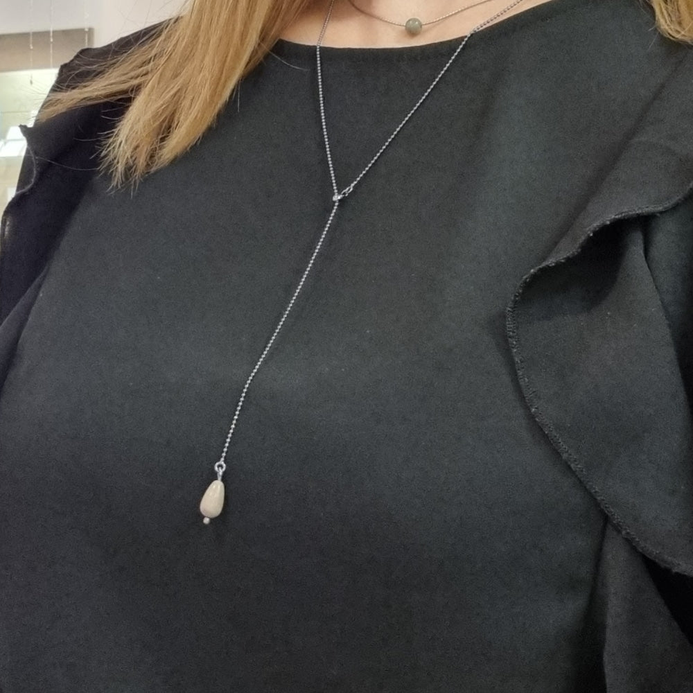 STRAND Droppe halsband with a teardrop beige stone pendant on a long silver chain worn over a black top