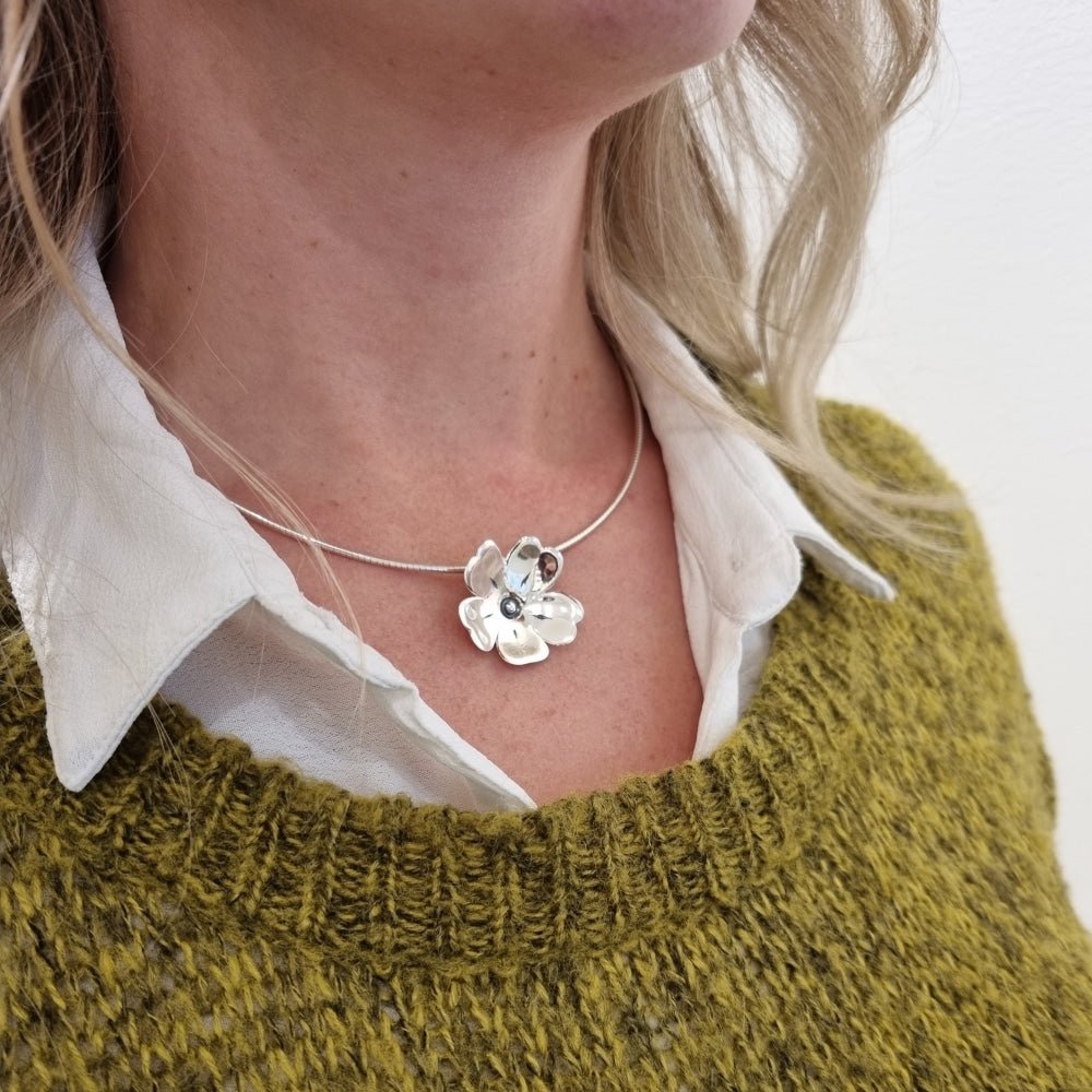 GULLVIVA halsband runt halsen på en person över vit skjorta och olivgrön tröja, blomformad silverberlock centralt.