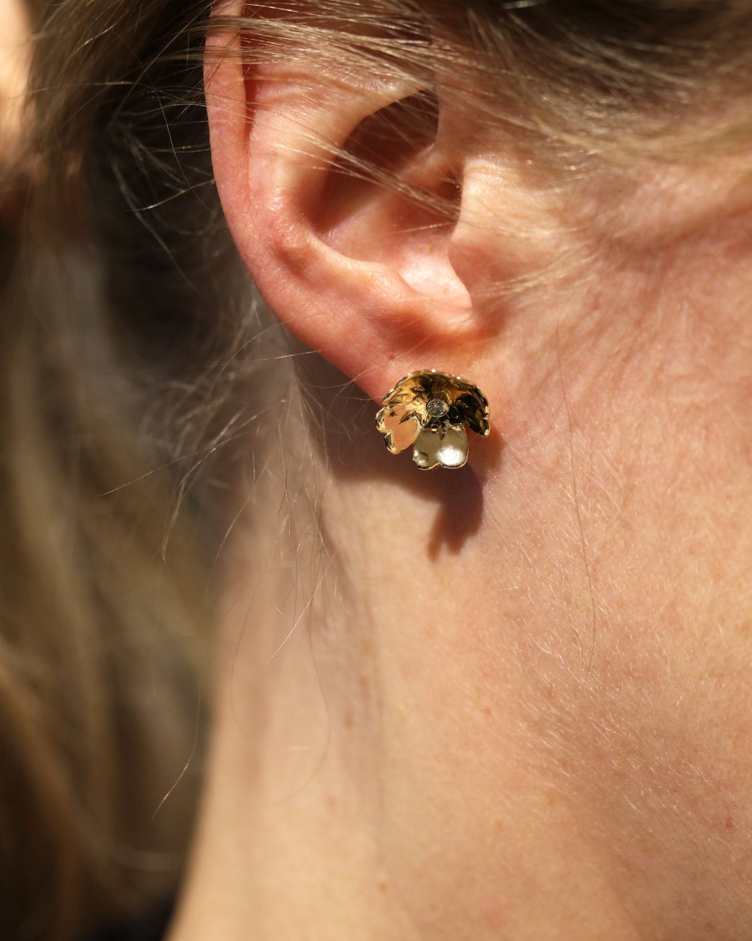 Öra med ett blomsterformat örhänge i 18K guld med diamant
