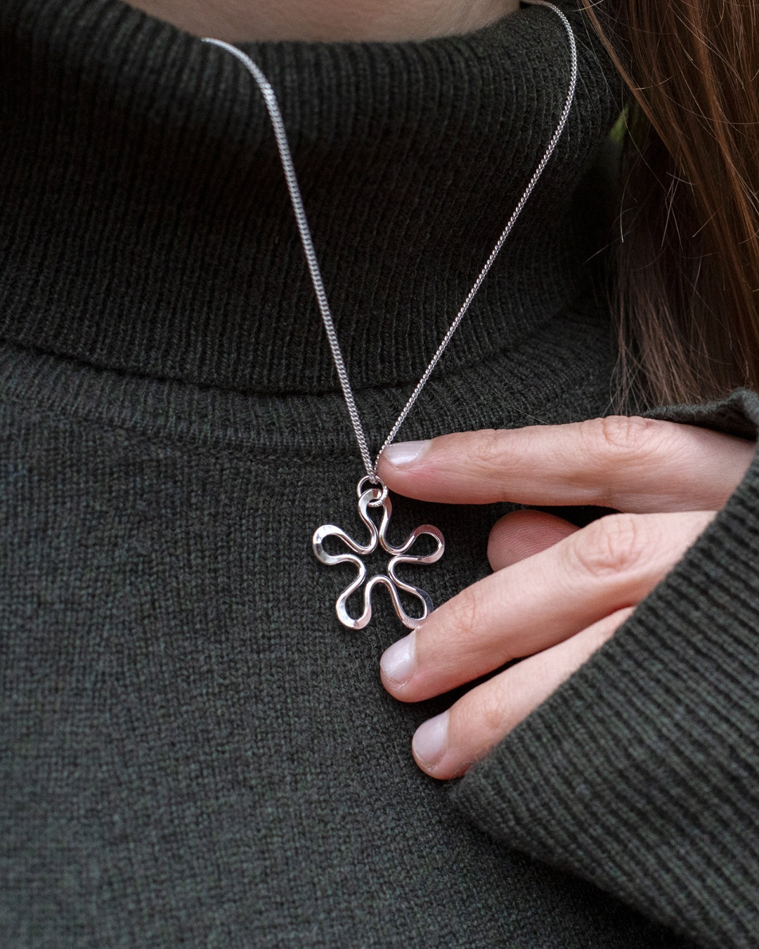 BLOMMAN halsband i sterlingsilver med blomformat hänge mot en mörk stickad tröja