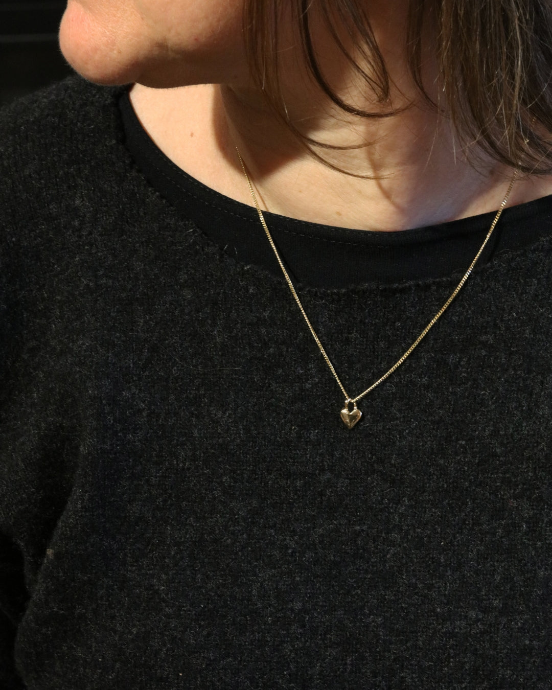 Modell bär ett 18K guld hjärtformigt hängsmycke på tunn kedja runt halsen