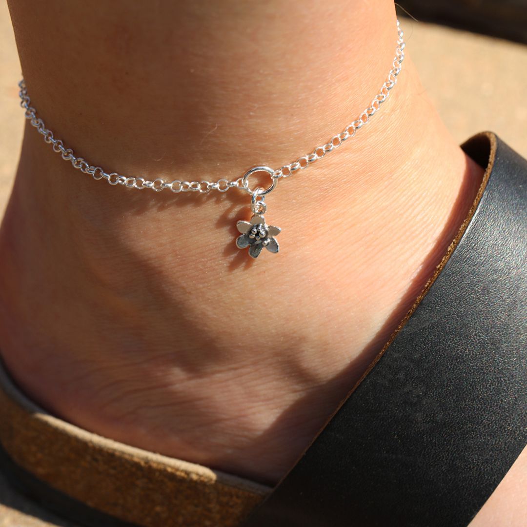 Close-up of 925 sterling silver anklet with a tiny flower charm worn on the ankle