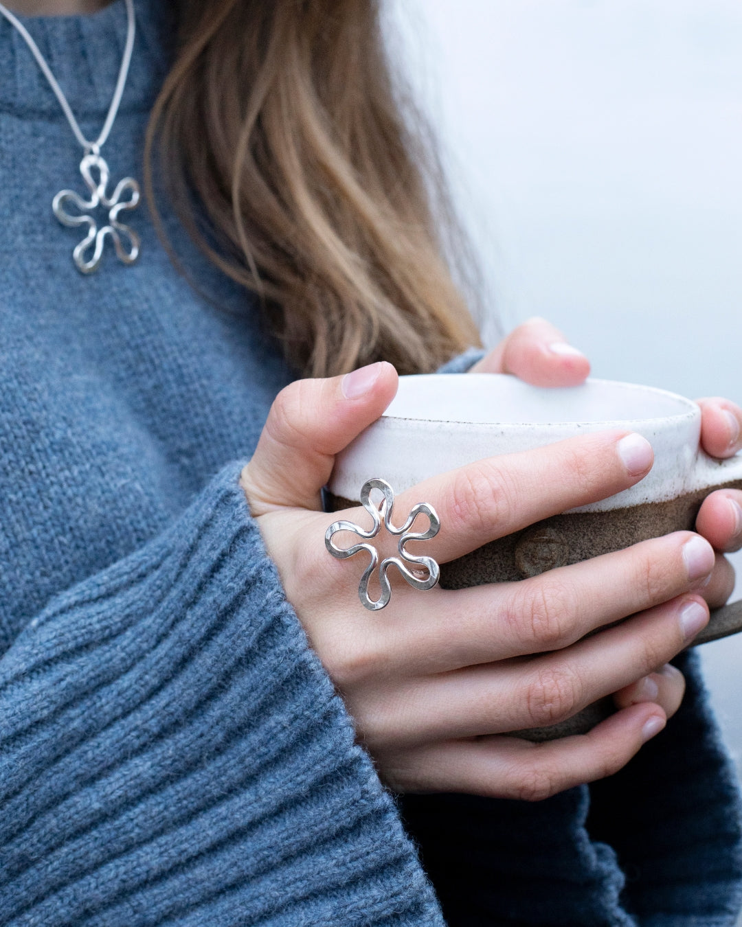 Model wearing BLOMMAN Elegant ring in silver with flower motif while holding a mug
