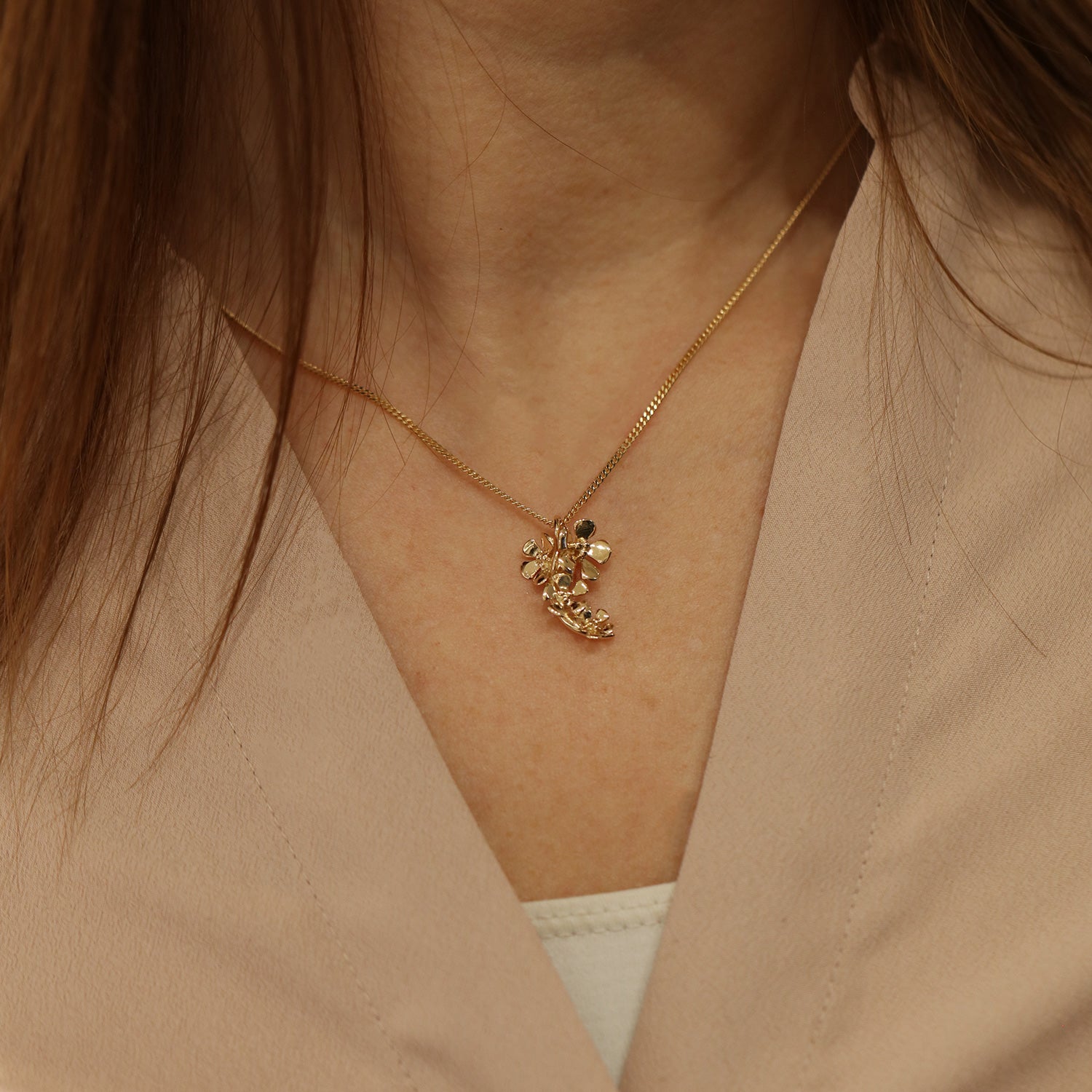 Close up of a gold flower cluster pendant on a thin chain at the collarbone