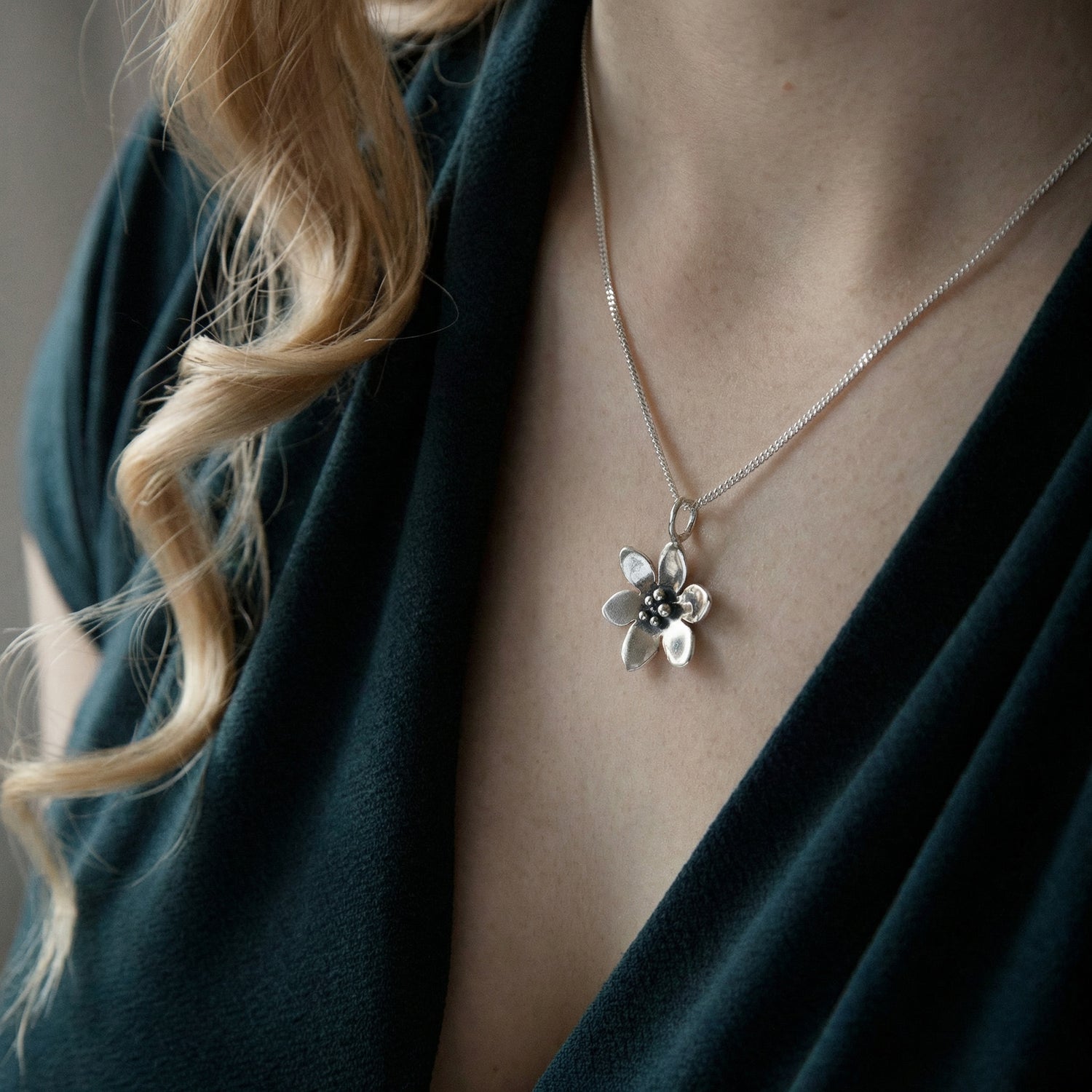 BLÅSIPPA necklace worn by a woman showing a silver flower pendant with petals