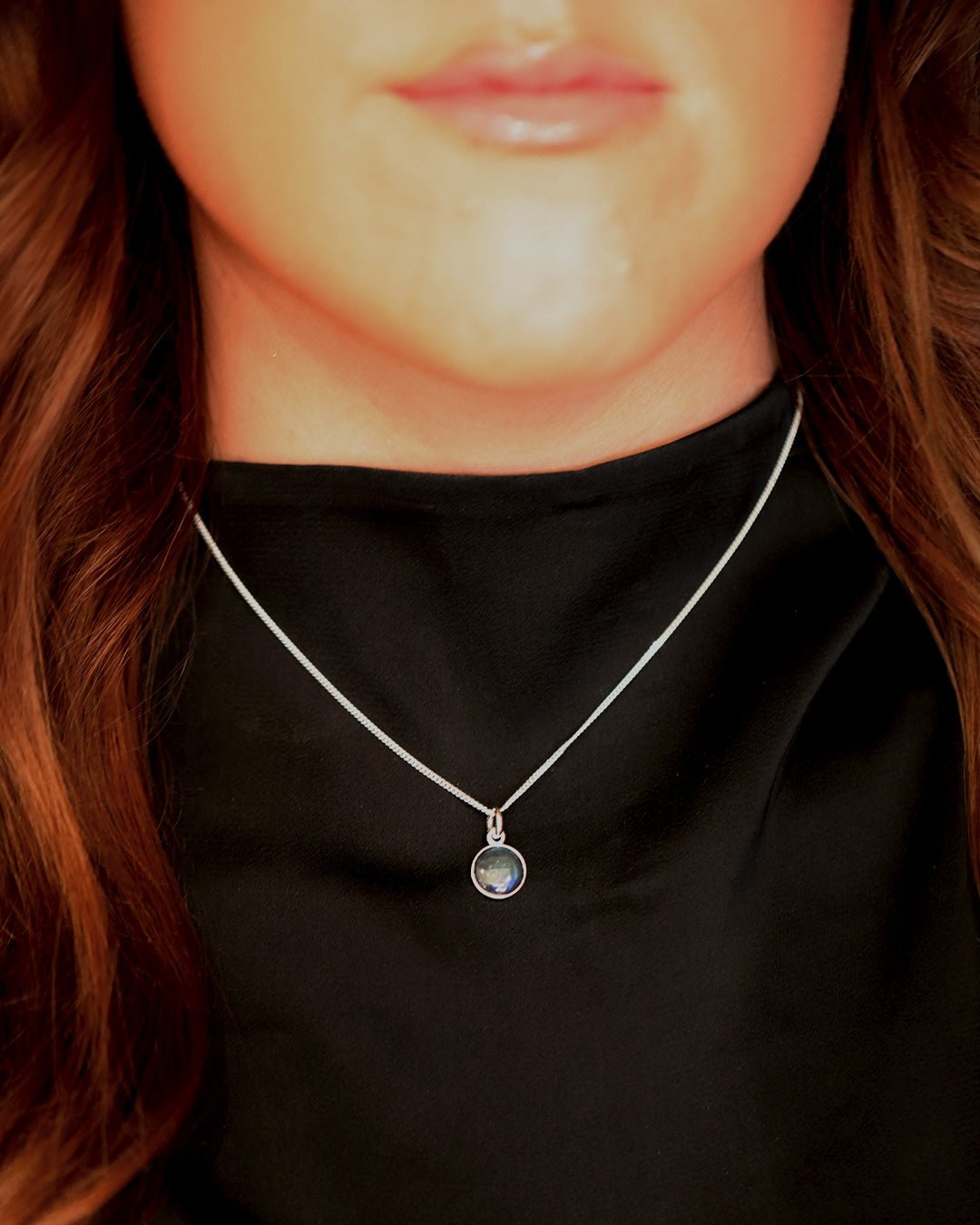 Round iridescent spektrolite pendant in a silver setting on a silver chain worn on a black top.