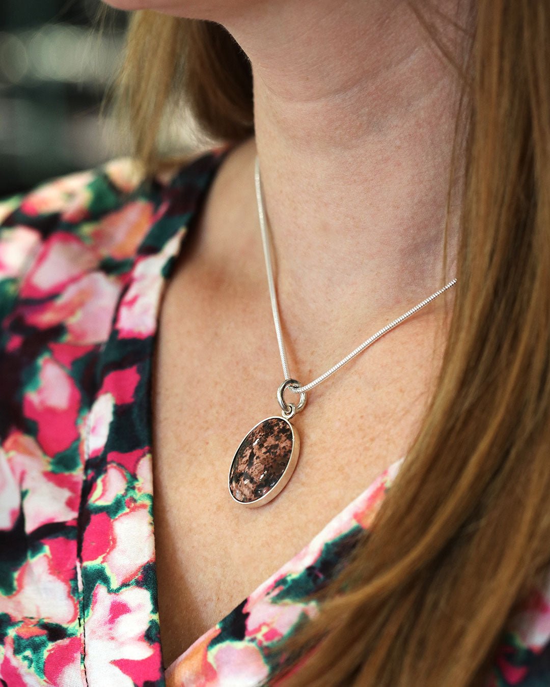 Silver chain with oval granite pendant worn at the neck by a person in a floral blouse