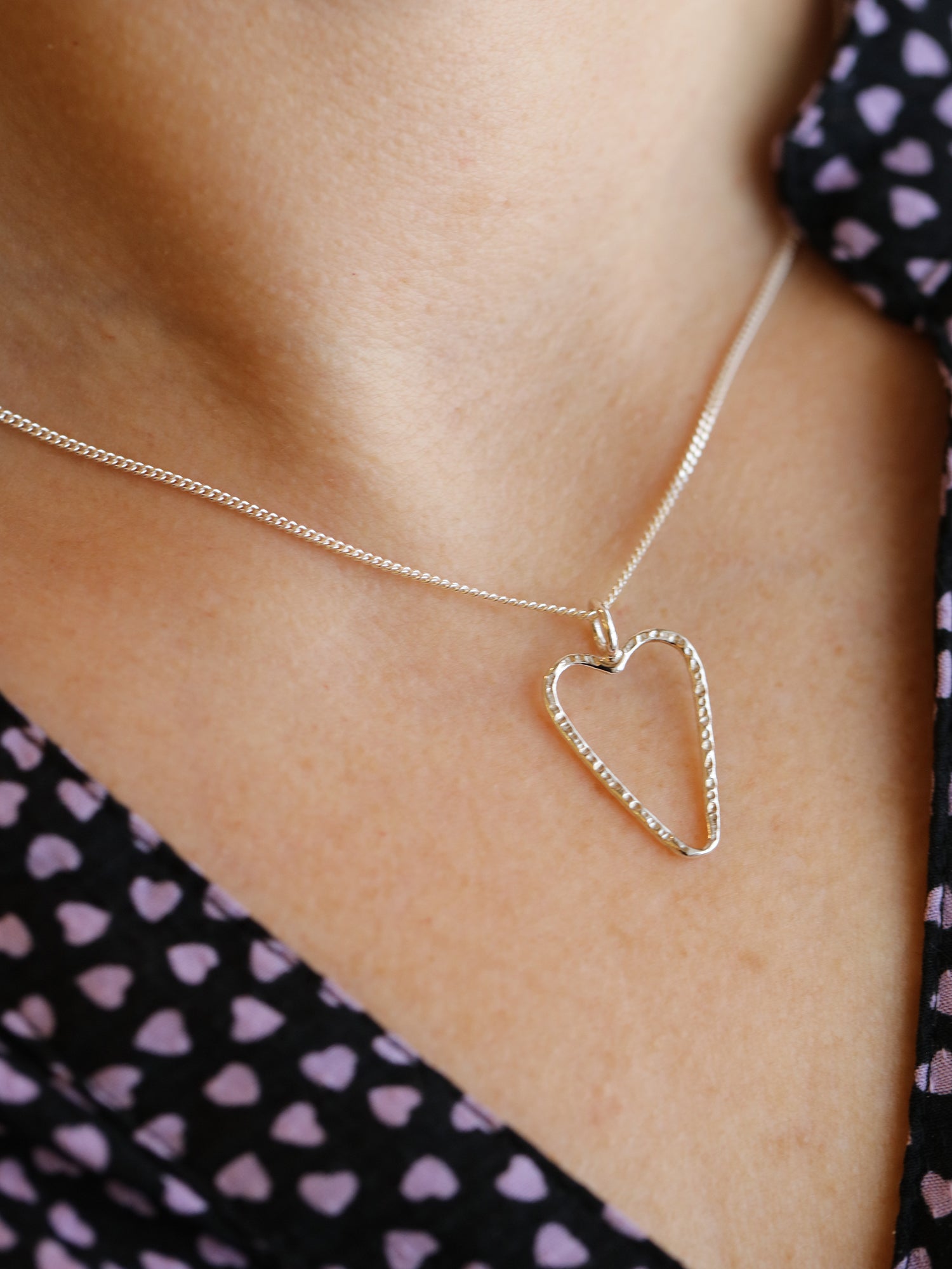 Närbild på öppet silverhjärta hänge på FRIENDS L halsband runt en persons hals