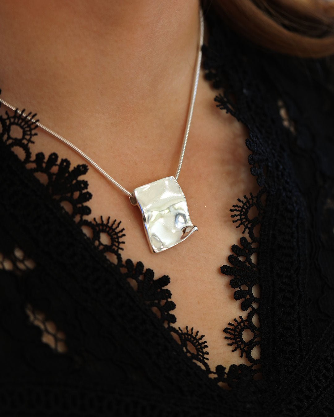 Model wearing PYRUS necklace with a polished silver plate pendant on a snake chain