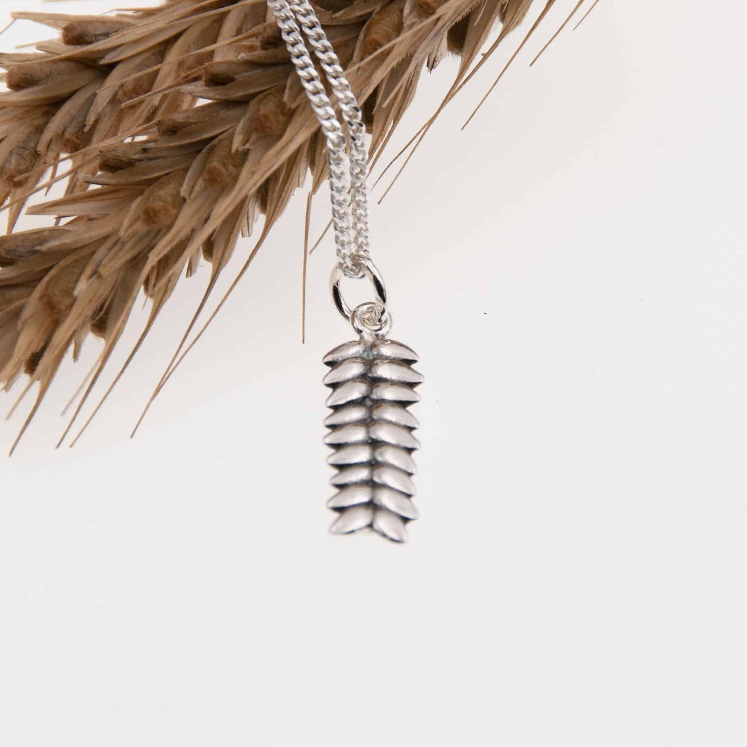 RÅG XS necklace with a silver pinecone pendant hanging from a chain.