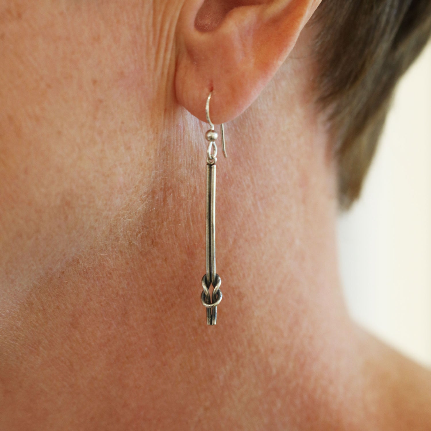 Närbild av RÅBANDSKNOP örhängen i sterlingsilver hängande från krok med knot nederst