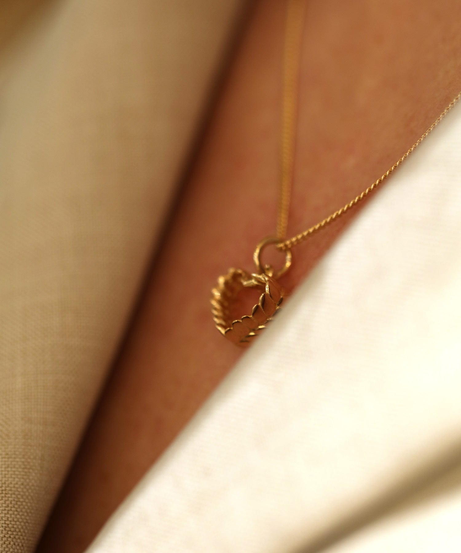 Close up of a gold heart pendant on a thin chain resting against the neck.
