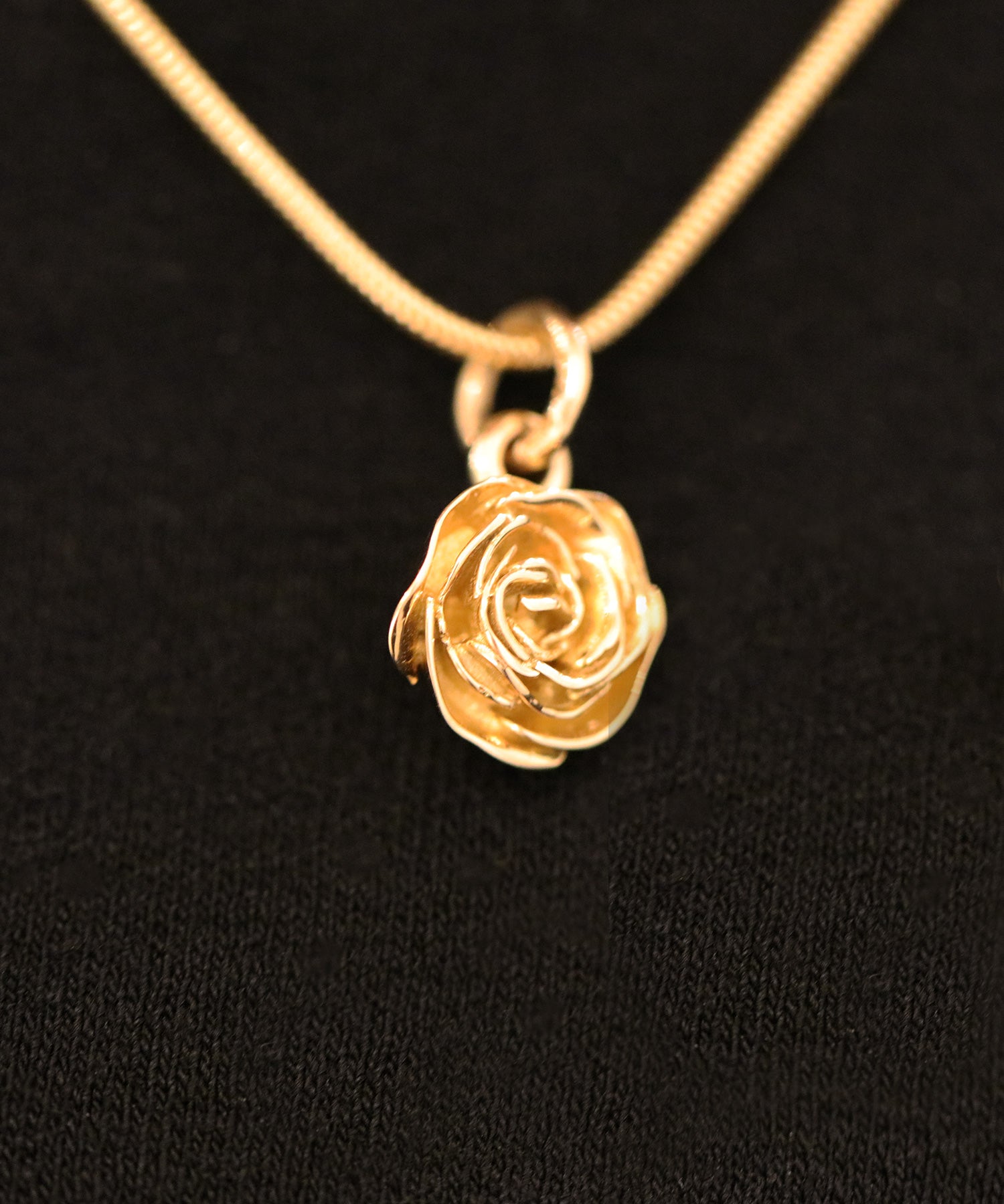 Närbild av rosformigt hänge på ROS 18K halsband med tunn kedja.