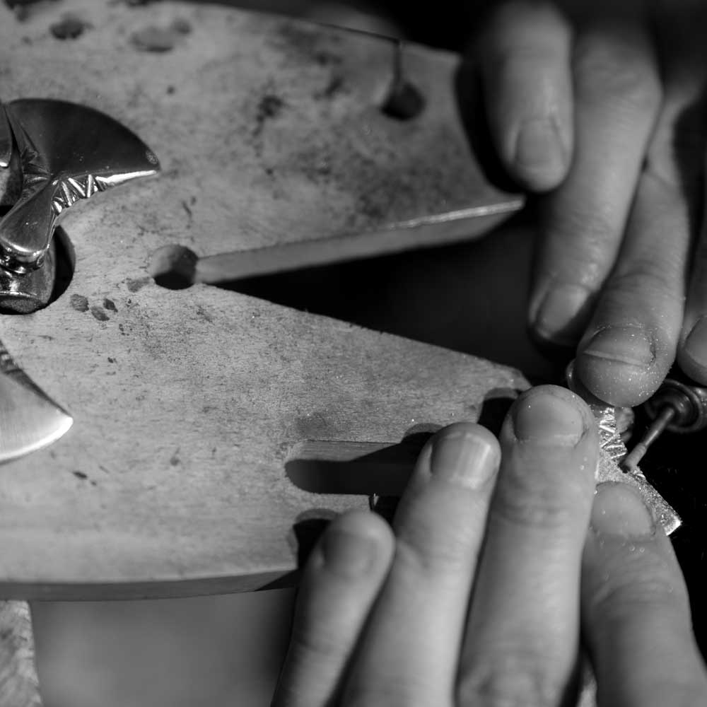Black and white close up of a jeweler shaping metal with a hammer on an anvil