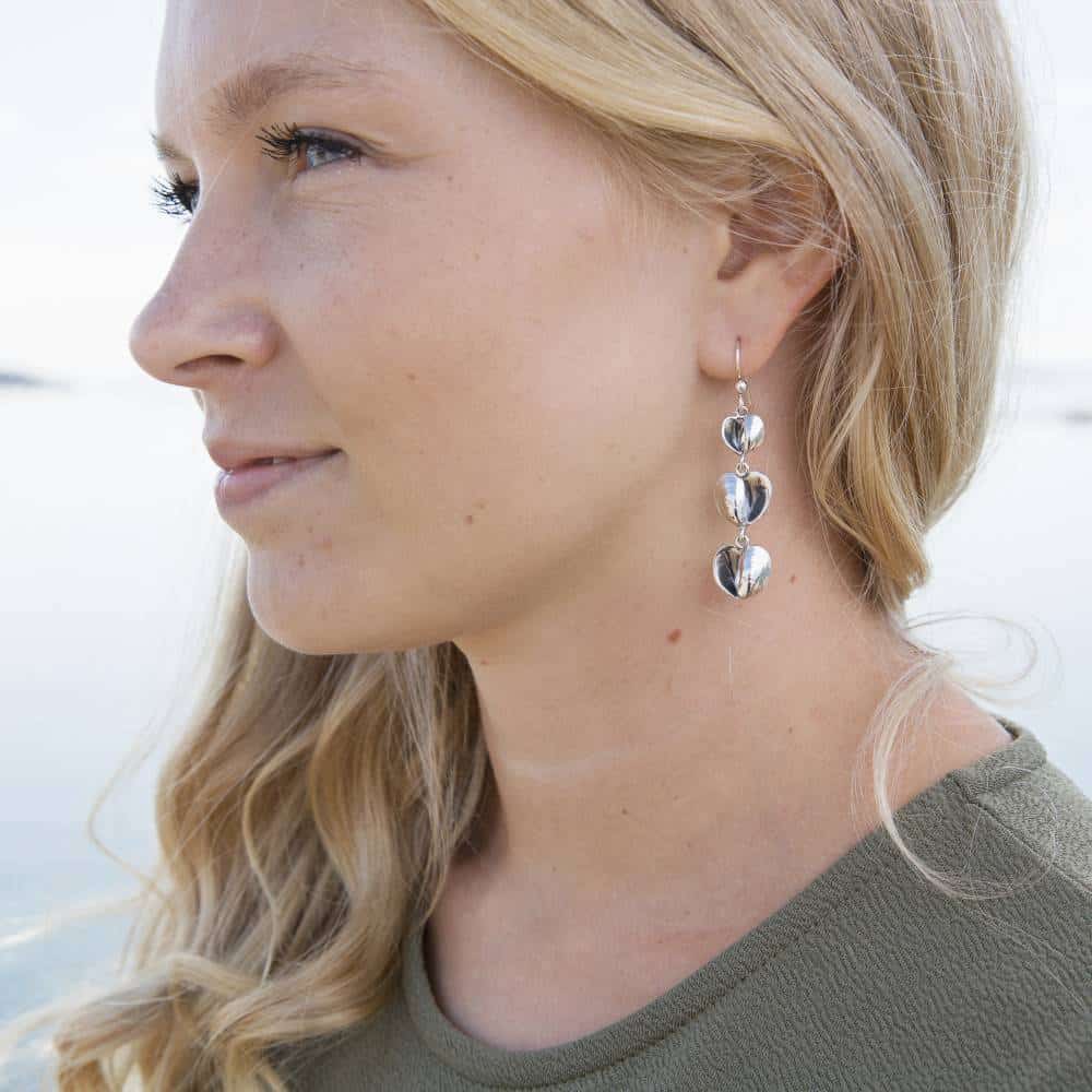 Profile of a woman wearing silver heart drop earrings with three linked hearts