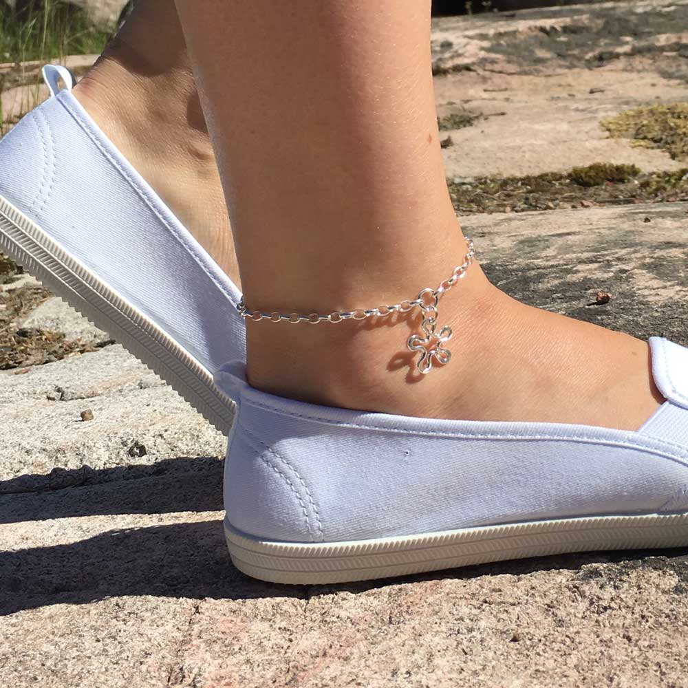 Silver BLOMMAN ankle bracelet with a flower charm worn around the ankle above a light blue sneaker.