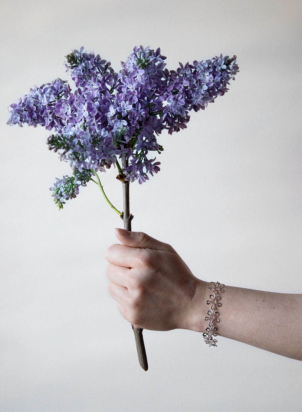 Hand holding a bouquet of purple lilac with a silver BLOMMAN armband on the wrist.