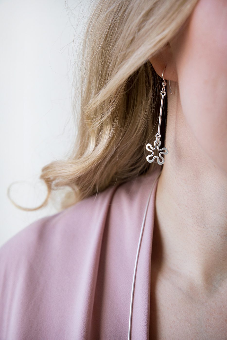 Long drop sterling silver BLOMMAN Duo earrings with a delicate multi petal flower pendant worn on the ear