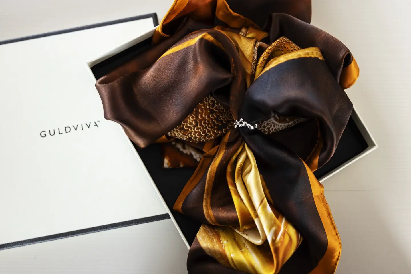 CELEBRATE Scarfring displayed in a gift box with a brown and gold scarf arranged around it