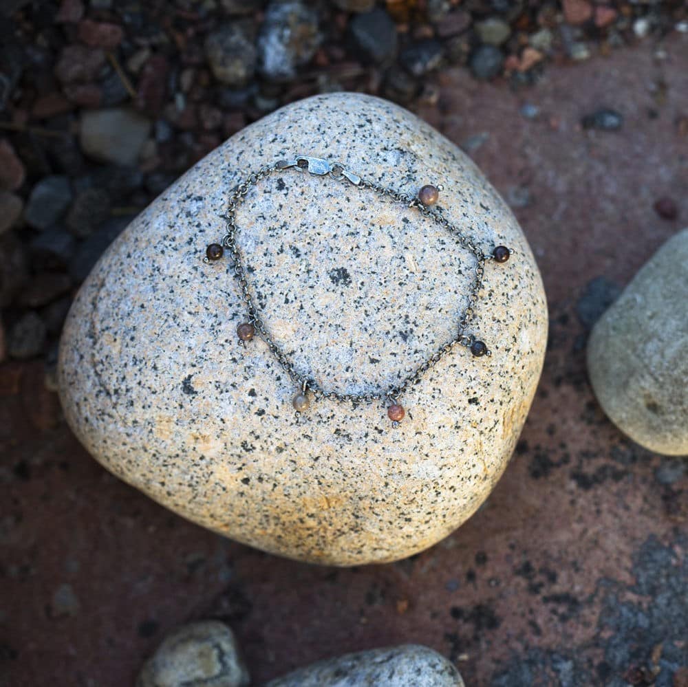 Silver armband med små färgade strandstenar vilar på en sten i naturen