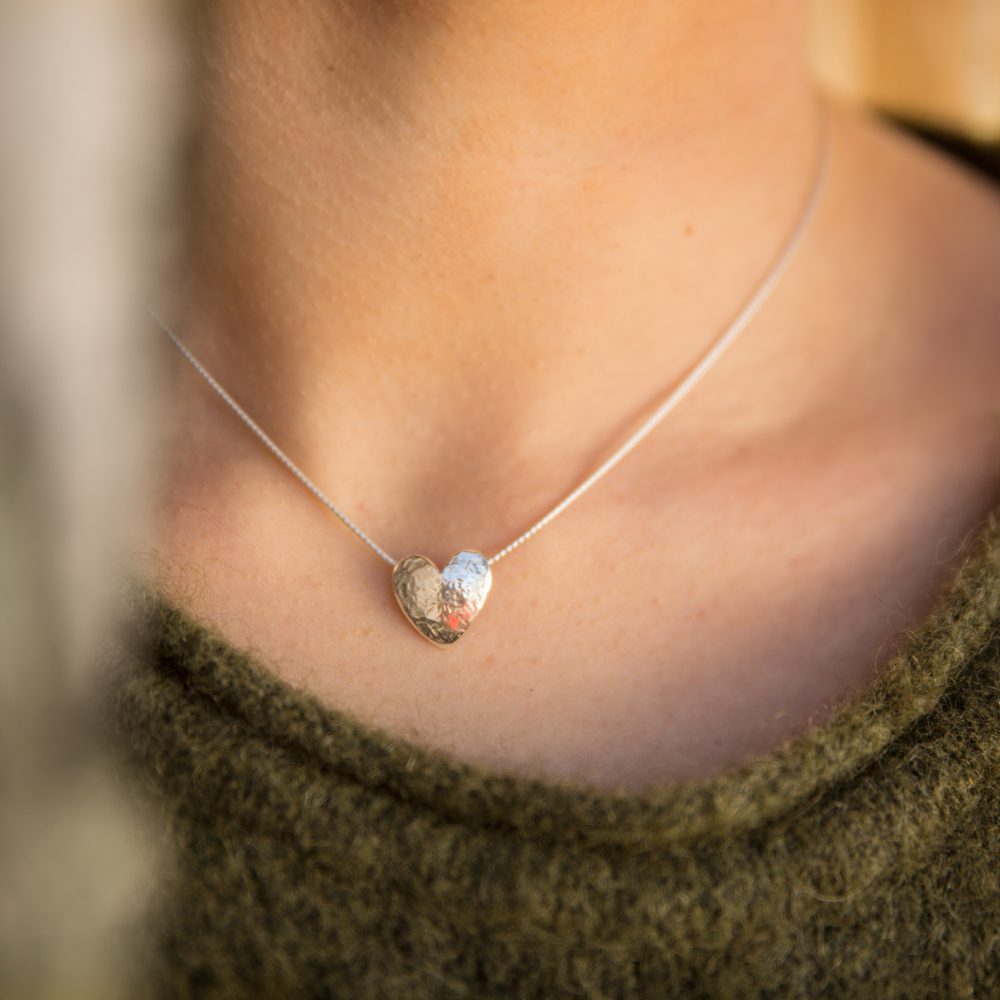 Person bär LOVE halsband med ett hjärtformat silverhänge med texturerad yta nära halsgropen