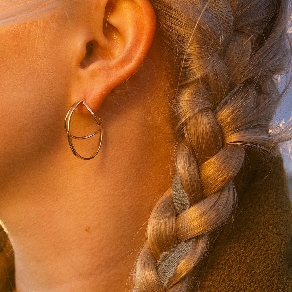 Ear close up wearing STORMSKÄRS MAJA FEST 18K gold hoop earring with braided hair in sunset light.