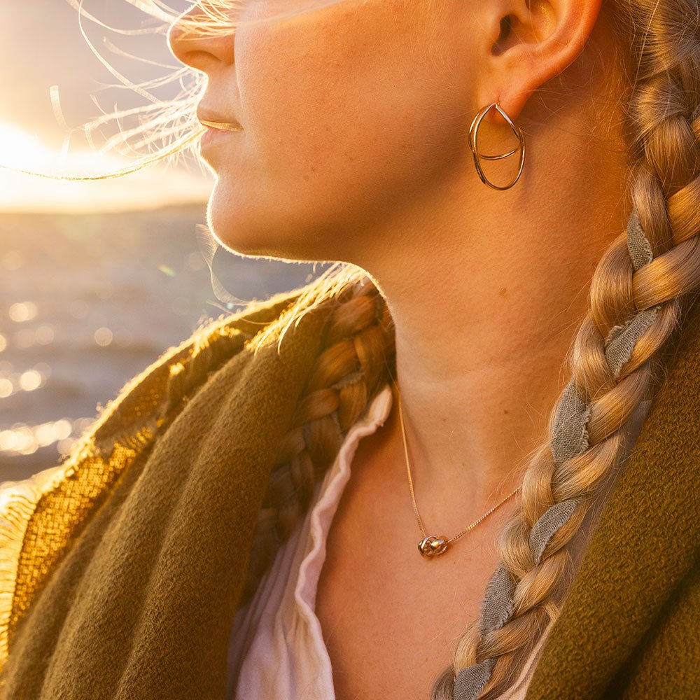 Close up of STORMSKÄRS MAJA S 18K gold necklace with a small pendant on a model during sunset.