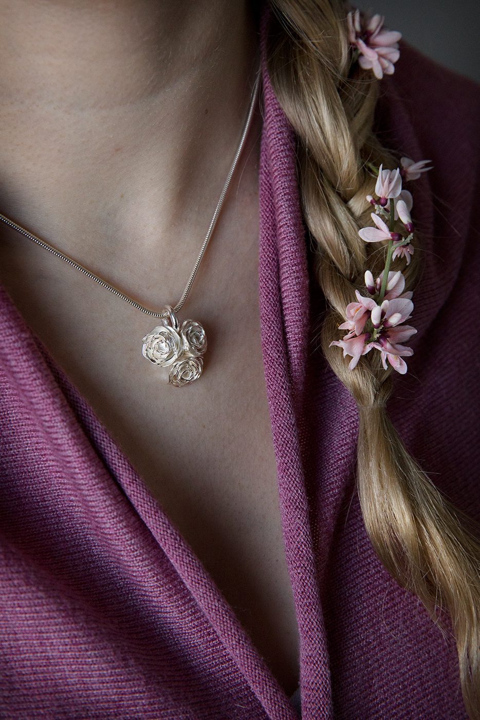 Silver necklace with three rose pendants on a slim chain worn near the neckline.