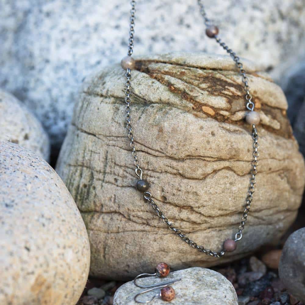 STRAND halsband i 925 sterling silver med små färgade stenar längs kedjan vilar över en sten