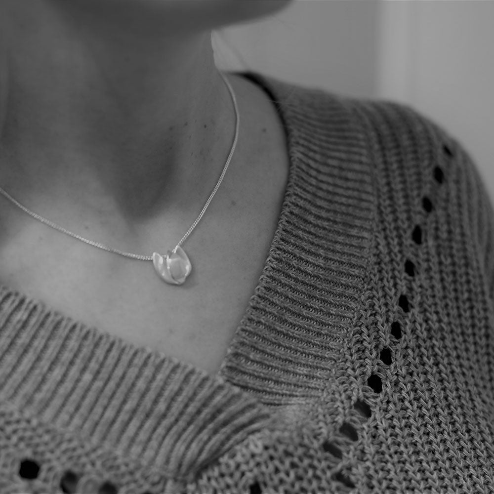 Model wearing a silver Tulpan Nova tulip pendant necklace on a knit sweater.