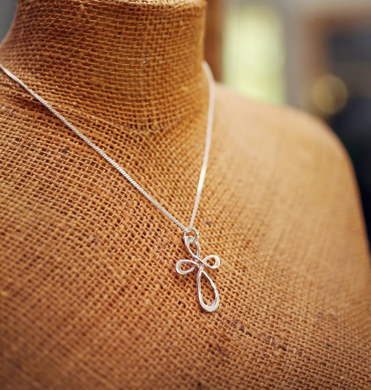 Silver chain necklace with a looped pendant displayed on a textured brown woven bust.