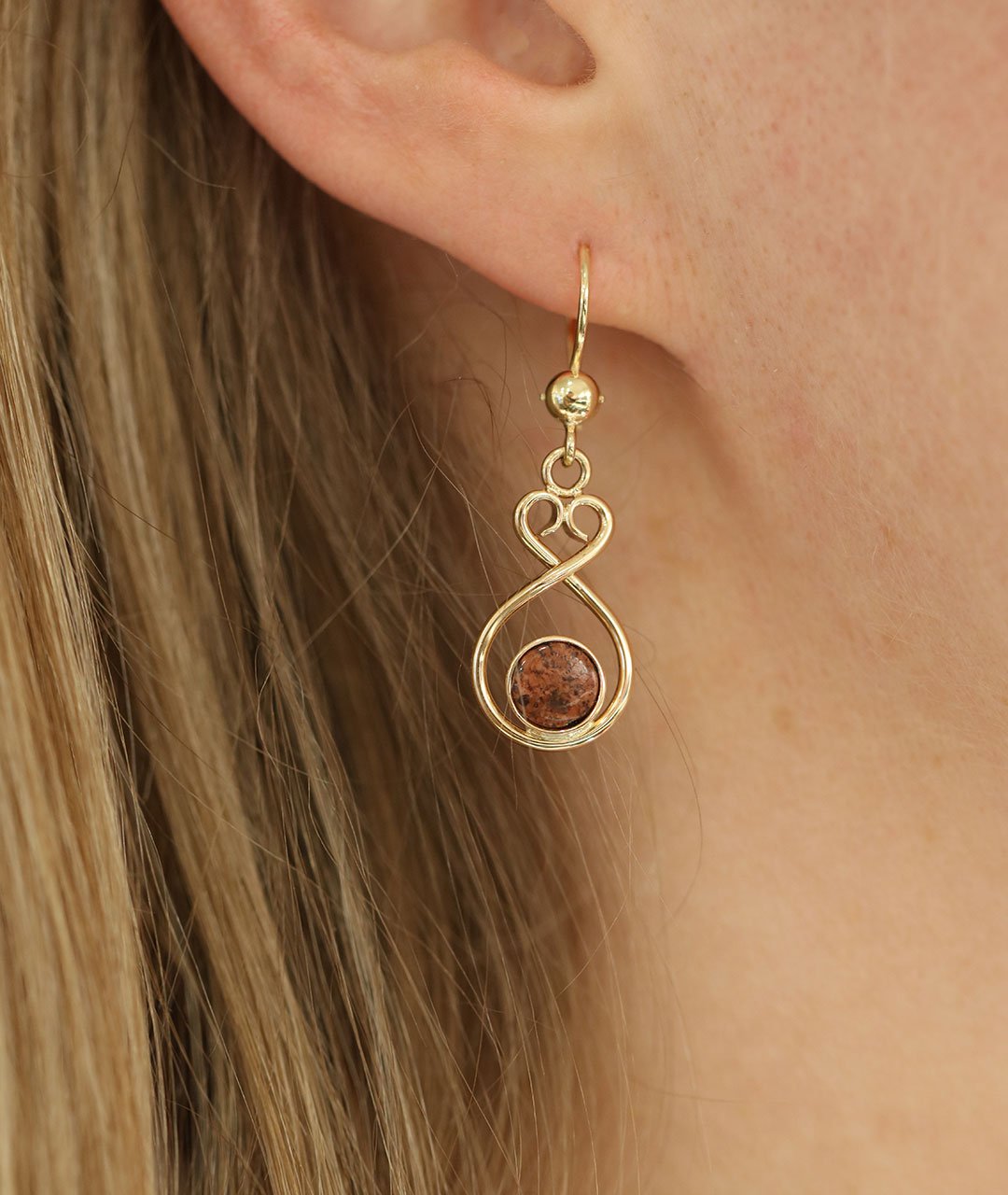 Pair of ÅLANDSHJÄRTA 18K gold earrings on hooks with red granite beads on a white background