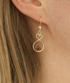 Pair of ÅLANDSHJÄRTA 18K gold earrings on hooks with red granite beads on a white background