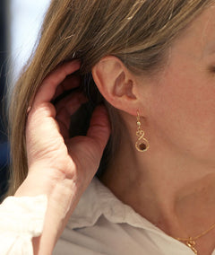 Gold ÅLANDSHJÄRTA 18K earring on ear featuring a heart shaped loop and red granite bead