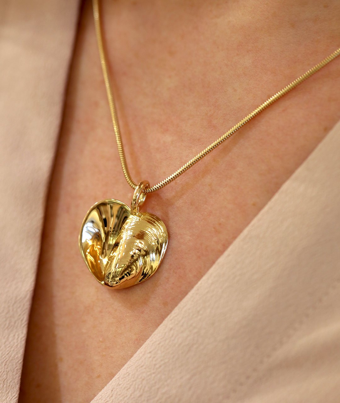 Two tone gold heart pendant necklace worn with a beige blouse on a person