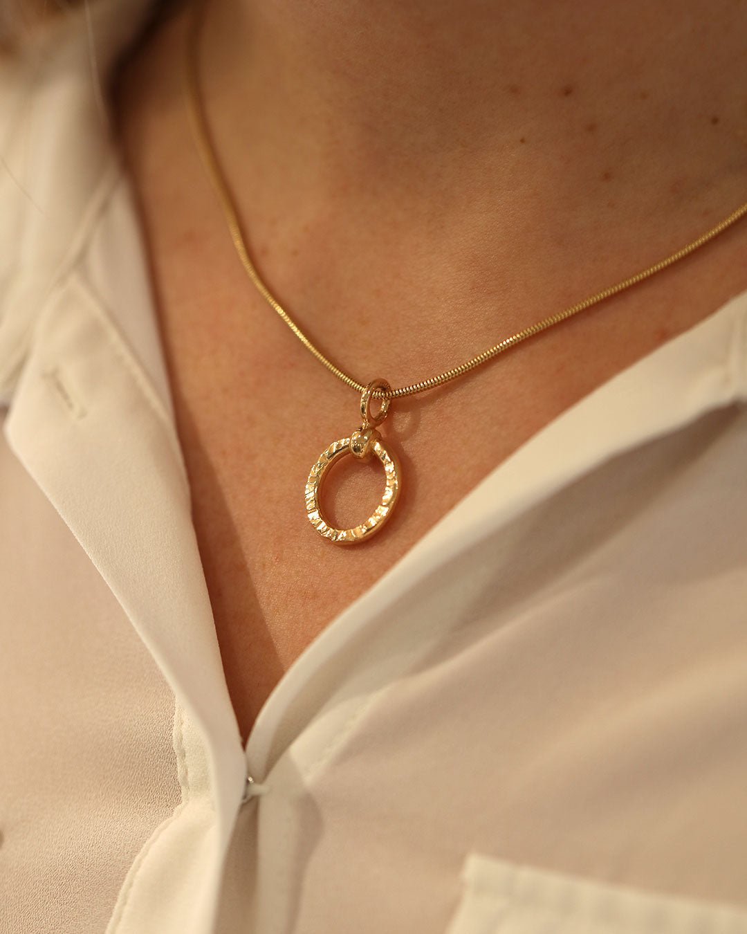 Närbild på CIRCLA halsbandet med cirkelformat hänge i 18K guld mot hud