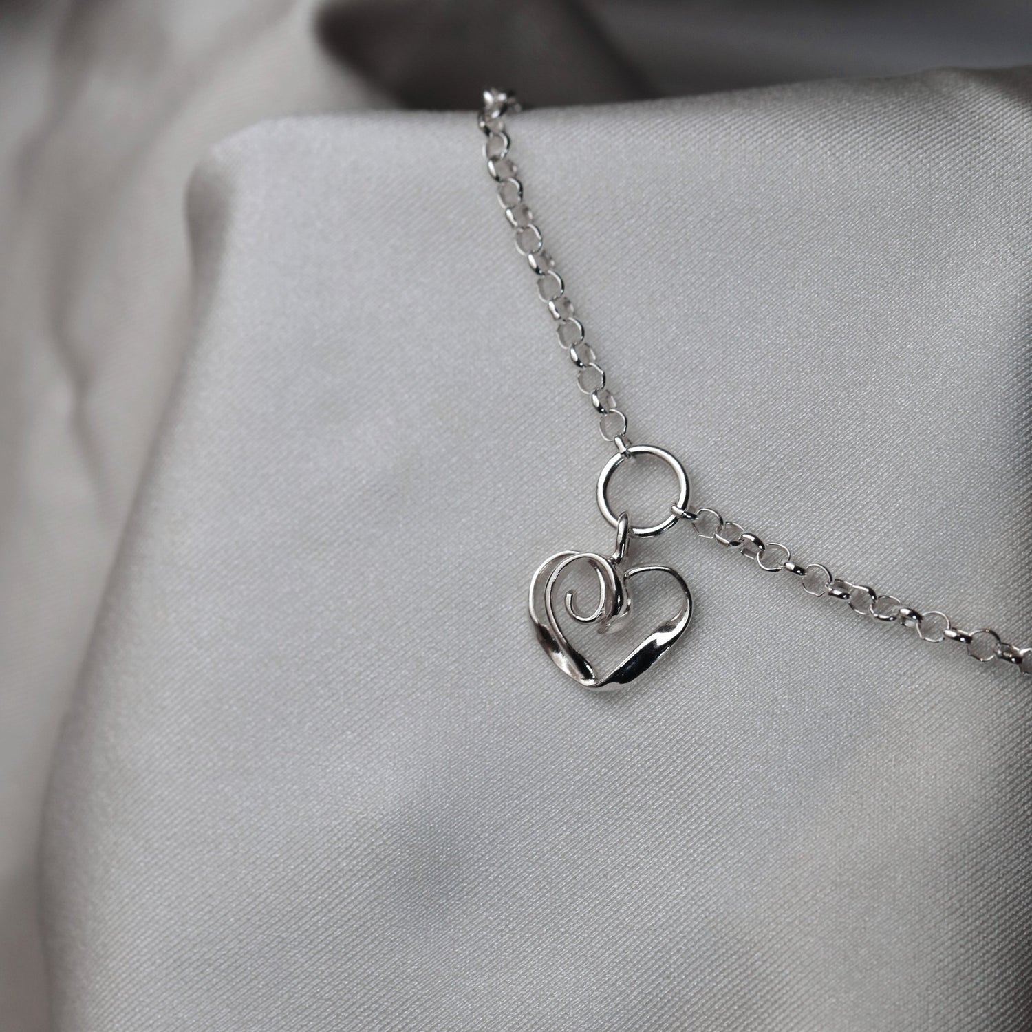 Närbild av silver armband med små ringformade länkar mot ljus tyg
