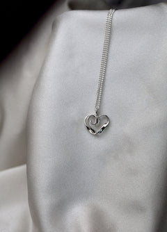 Close-up of a sterling silver chain necklace with a heart pendant on a light fabric backdrop