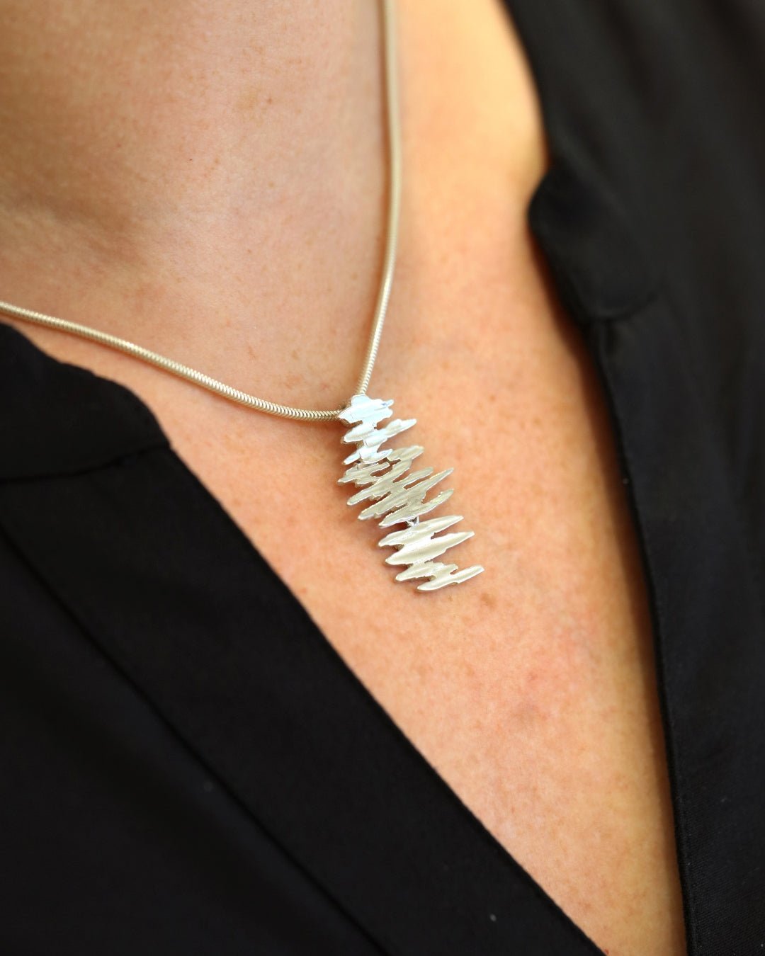 Model wearing the ALANDICA necklace with stacked silver pendant on a black blouse