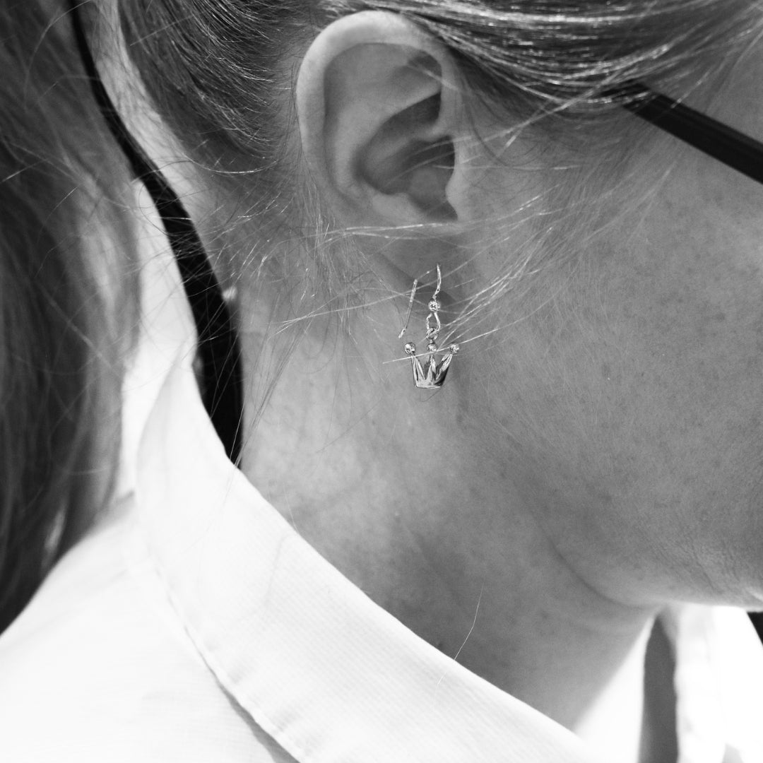 Close-up of silver crown drop earring on ear showing hook and crown shape