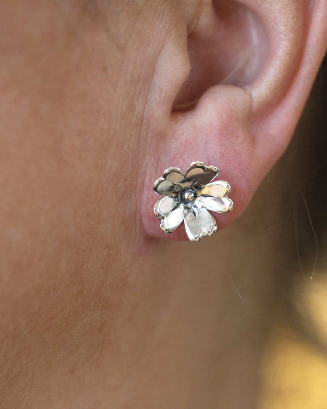 Närbild på GULLVIVA blomformade örhängen i sterlingsilver i modellens öra