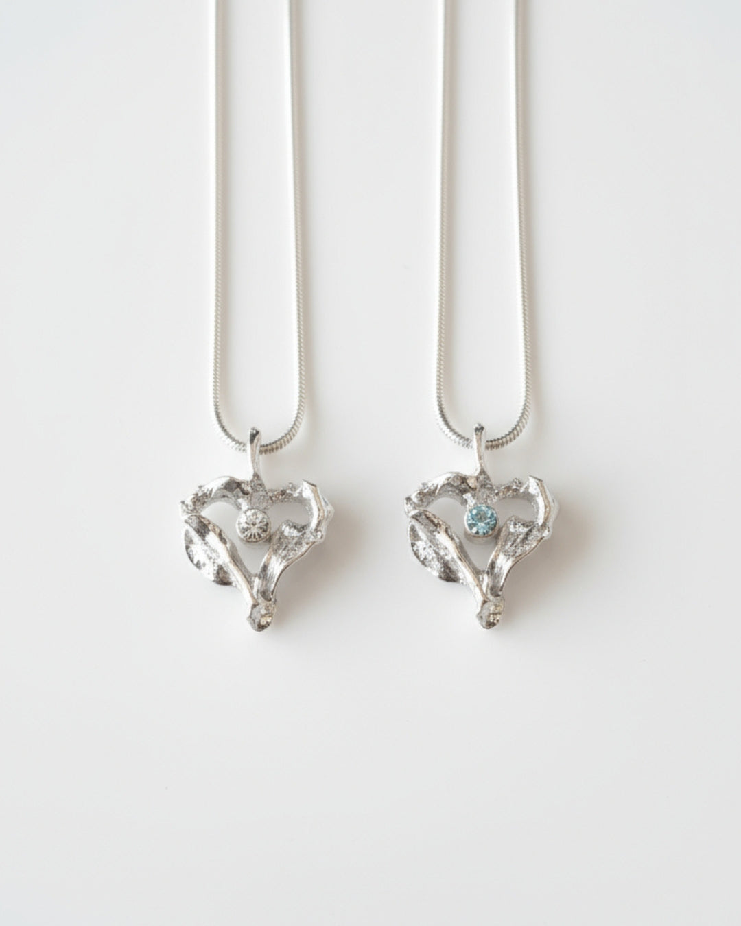 Två silver hjärtformade hängen i presentlåda, ena med klar sten och andra med aquamarin.