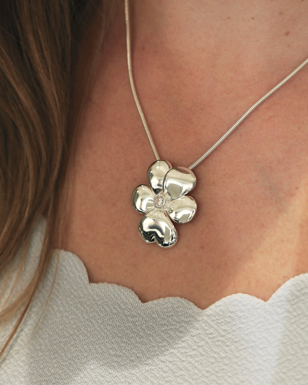 Silver flower pendant necklace with a cubic zirconia center on a snake chain worn at the neckline.