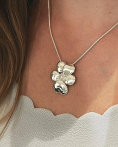 Silver flower pendant necklace with a cubic zirconia center on a snake chain worn at the neckline.