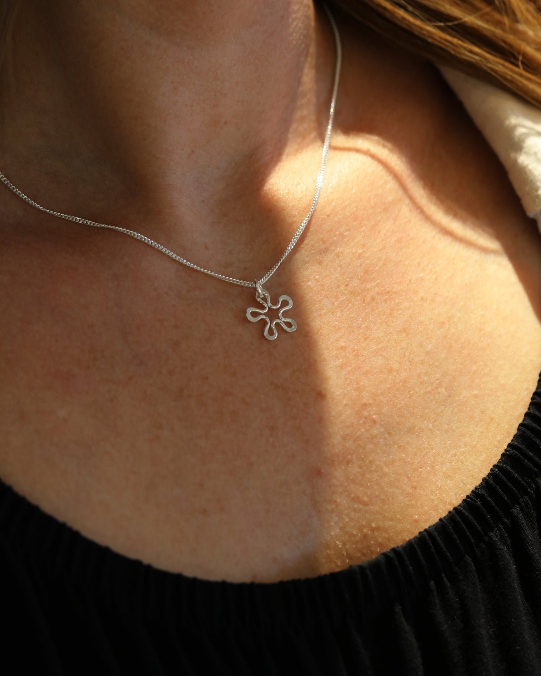 Close-up of BLOMMAN XS necklace showing the silver flower pendant at the neck