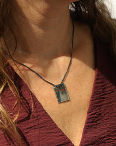 Close up of irregular rectangular silver ID bricka pendant on a dark chain against skin