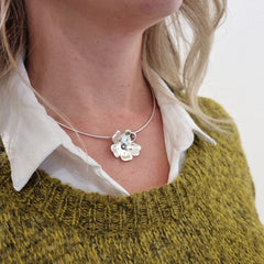 GULLVIVA halsband runt halsen på en person över vit skjorta och olivgrön tröja, blomformad silverberlock centralt.