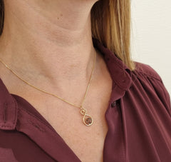 Modell bär ÅLANDSHJÄRTA halsband i guld med röd granit i mitten runt halsen.