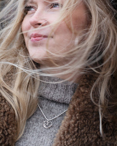 Close-up of a smiling woman wearing the silver heart pendant necklace over a gray knit turtleneck